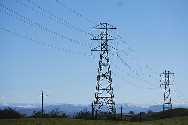 A couple powerlines against blue skies and mountains.