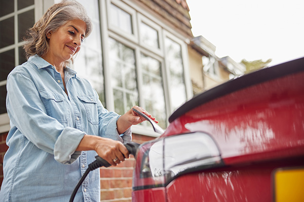 Older woman plugs in her ev while smiling