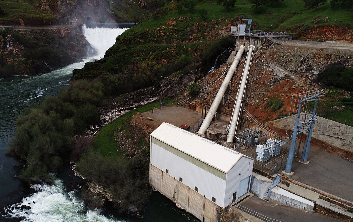 A canal overpours into river and a powerhouse is around the bend.