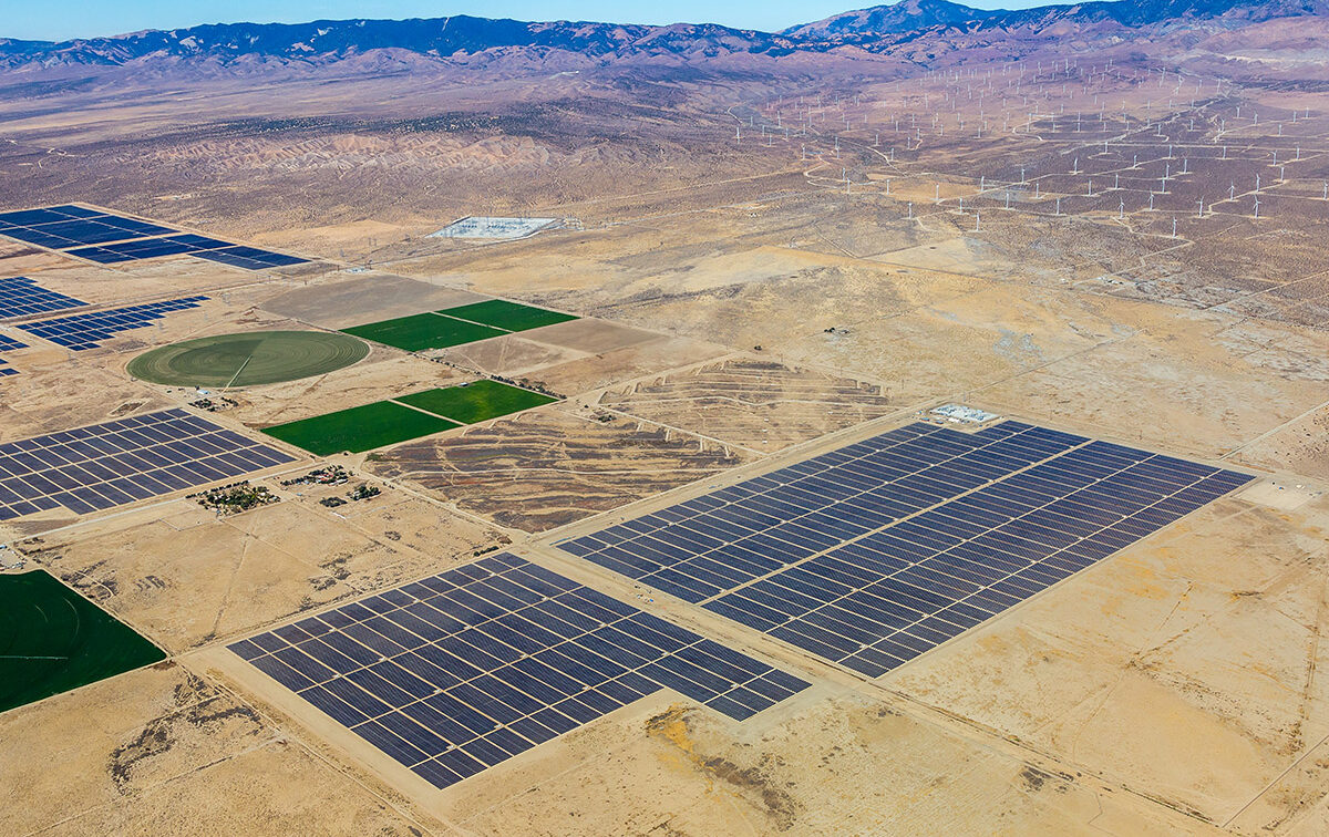 Aerial view of solar panels and wind turbines in a mountainous region.