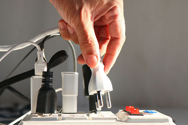 Man's hand is plugging an electrical plug into an extension cord socket.