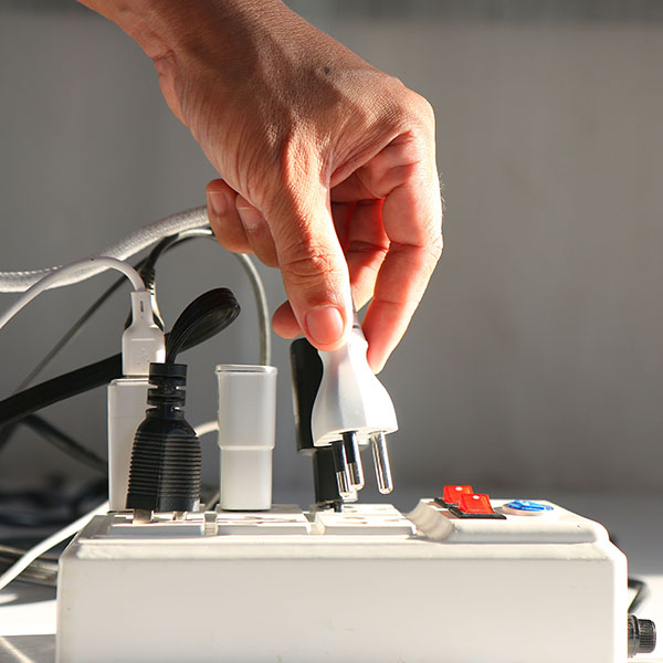 Man's hand is plugging an electrical plug into an extension cord socket.