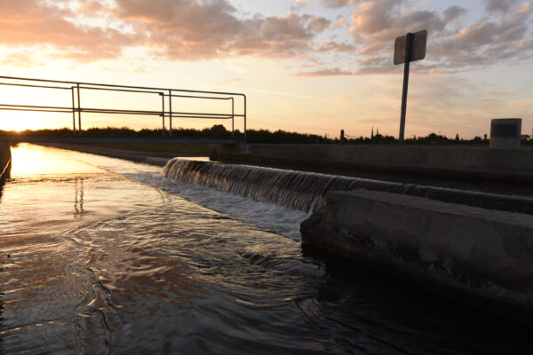 Irrigation canal drop with water flowing and sunset off in the distance.