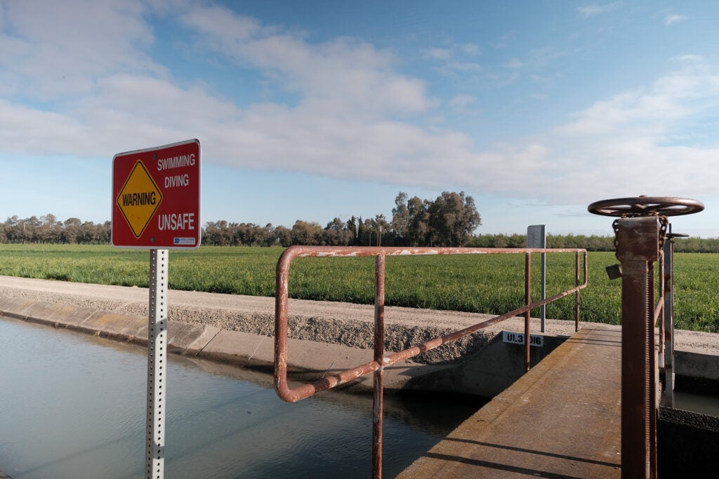 Walking bridge over irrigation canal with Warning sign that reads "swimming, diving unsafe."