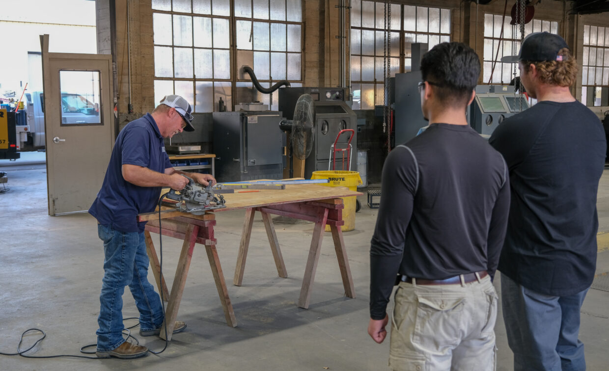 Presenter shows group of students how to use a saw.