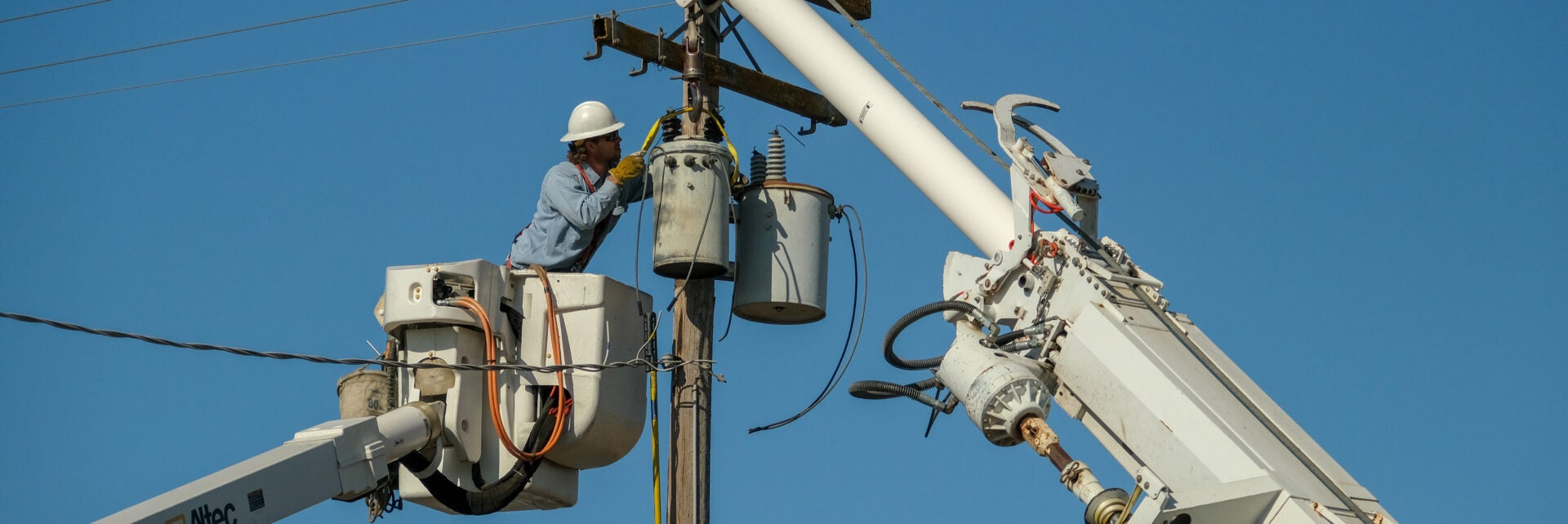 Electrical lineworker in bucket truck repairing a transformer on a pole.